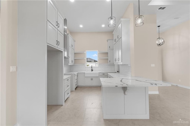 kitchen featuring pendant lighting, white cabinets, a kitchen breakfast bar, sink, and light stone counters