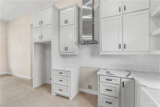 kitchen with light stone counters, white cabinetry, tasteful backsplash, and wall chimney range hood