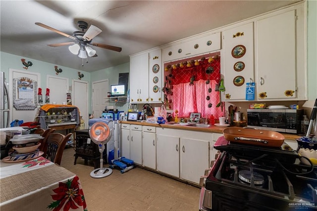 kitchen featuring white cabinets, range with gas cooktop, stainless steel microwave, light floors, and a sink