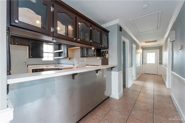 kitchen with a kitchen bar, kitchen peninsula, dark brown cabinets, crown molding, and light tile patterned floors