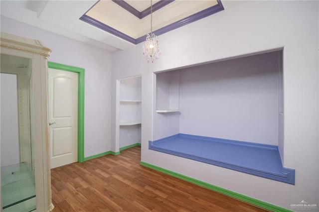 interior space with hardwood / wood-style flooring, a notable chandelier, a raised ceiling, and crown molding