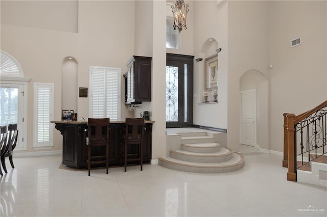 tiled foyer entrance with bar area, a towering ceiling, and an inviting chandelier