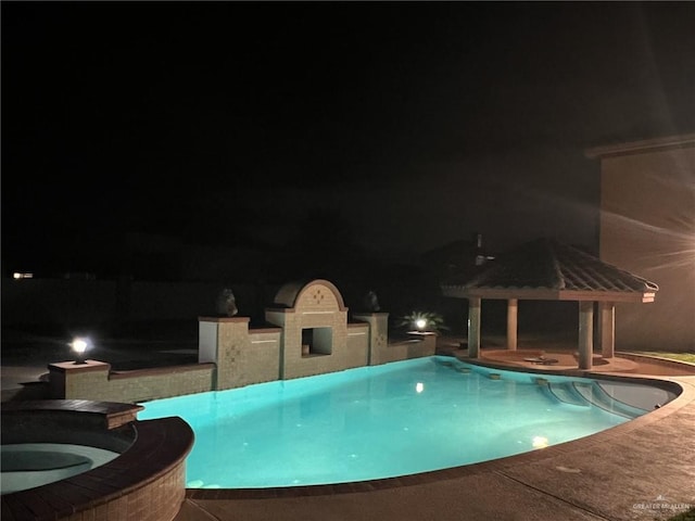 pool at night with a gazebo and an in ground hot tub