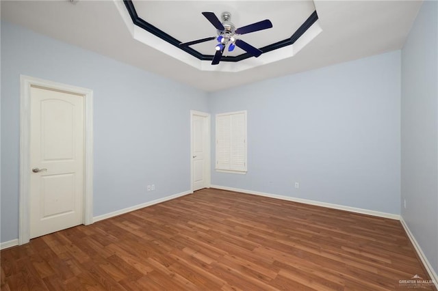 empty room with hardwood / wood-style floors, ceiling fan, and a tray ceiling