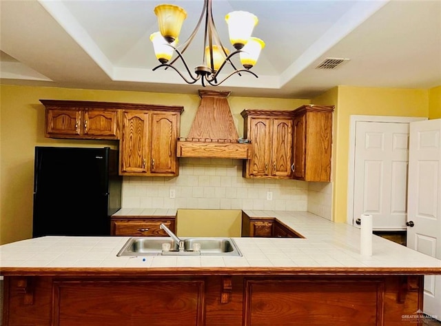 kitchen featuring black fridge, a raised ceiling, and tile counters