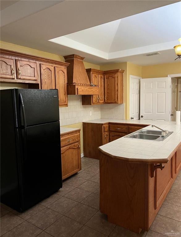 kitchen with tile countertops, premium range hood, black fridge, sink, and tasteful backsplash