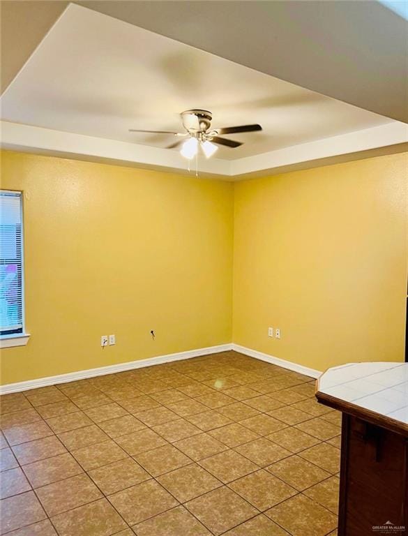 spare room featuring tile patterned floors, ceiling fan, and a tray ceiling