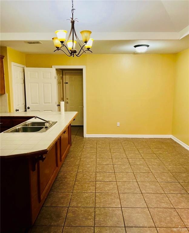 kitchen featuring sink, hanging light fixtures, an inviting chandelier, an island with sink, and light tile patterned floors