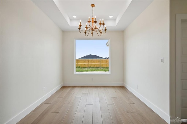 403 Faith Dr, La Feria, TX 78559 - spare room featuring light wood-style flooring, a raised ceiling, a notable chandelier, and baseboards