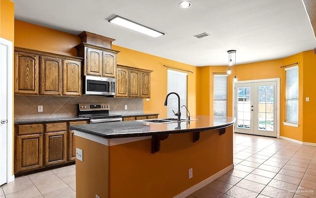 1915 Bunting Ln, Mission, TX 78572 - kitchen featuring appliances with stainless steel finishes, decorative backsplash, light tile patterned flooring, a kitchen island with sink, and french doors