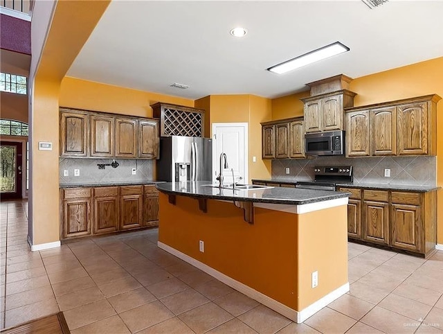 1915 Bunting Ln, Mission, TX 78572 - kitchen featuring stainless steel appliances, light tile patterned floors, backsplash, a kitchen breakfast bar, and an island with sink