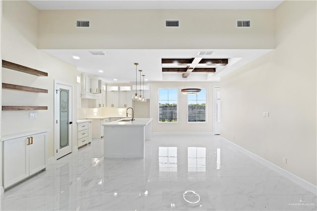 kitchen featuring a kitchen island with sink, coffered ceiling, white cabinets, sink, and hanging light fixtures