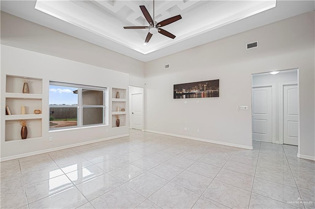 empty room featuring a tray ceiling, built in features, and ceiling fan