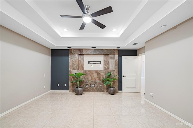 empty room with ceiling fan and a tray ceiling