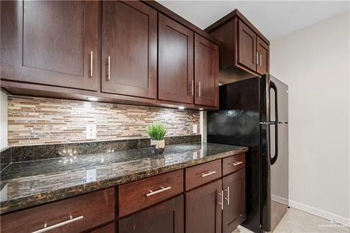 kitchen featuring backsplash, black refrigerator, light tile patterned flooring, and dark stone countertops