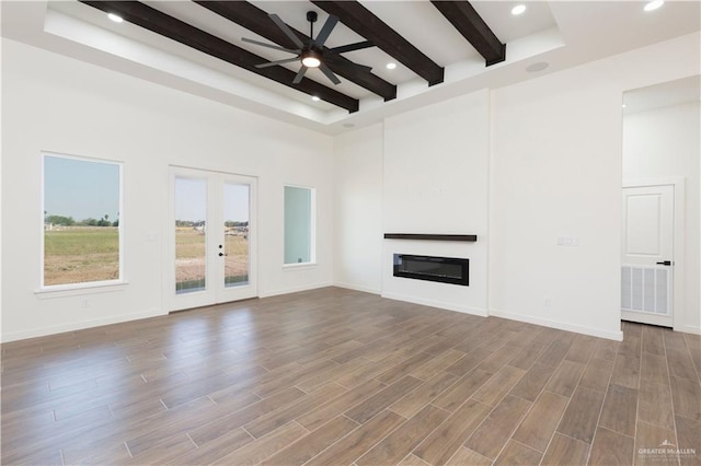 unfurnished living room with ceiling fan, beam ceiling, and a high ceiling