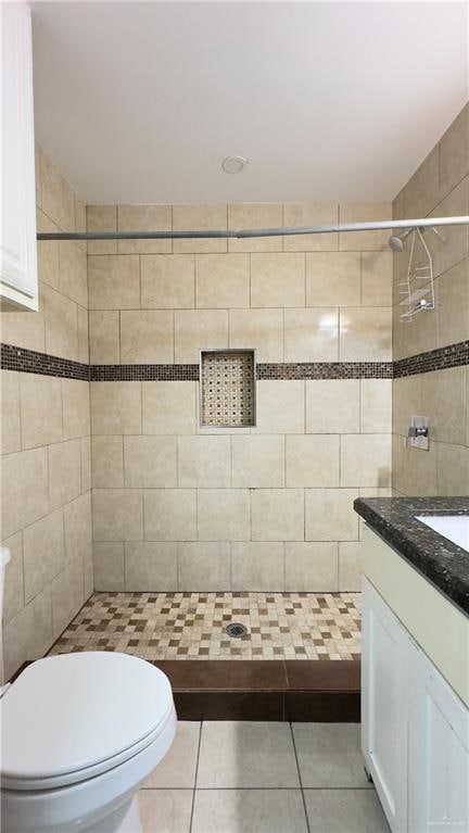 bathroom featuring tile patterned flooring, a tile shower, vanity, and toilet