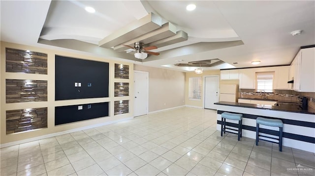 kitchen featuring a tray ceiling, ceiling fan, white fridge, white cabinetry, and light tile patterned flooring