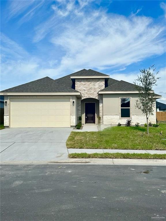 1804 Hailey St, San Juan, TX 78589 - view of front of property featuring driveway, a front yard, stone siding, a shingled roof, and a garage