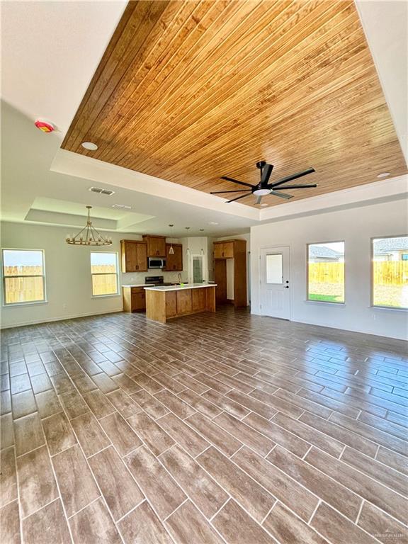 1804 Hailey St, San Juan, TX 78589 - unfurnished living room featuring visible vents, baseboards, a raised ceiling, ceiling fan with notable chandelier, and wood ceiling