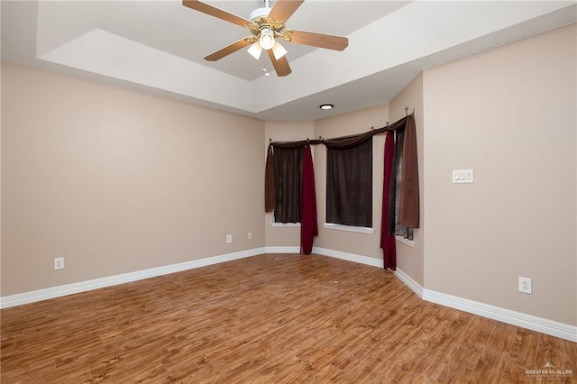 empty room with a raised ceiling, ceiling fan, and hardwood / wood-style floors