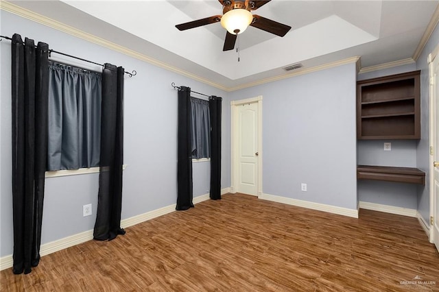 unfurnished bedroom with hardwood / wood-style floors, ceiling fan, a raised ceiling, and ornamental molding