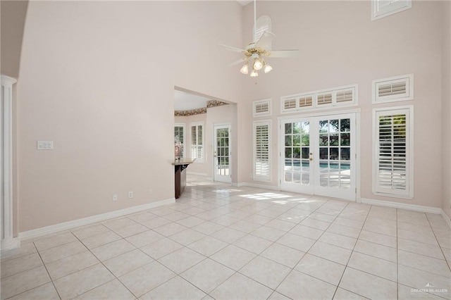 unfurnished living room with ceiling fan, french doors, light tile patterned floors, and a high ceiling