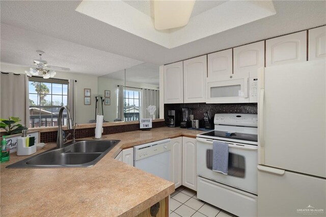 kitchen featuring a peninsula, white appliances, a sink, and white cabinetry