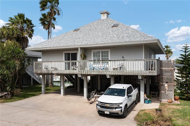 rear view of house with stairs, a carport, a shingled roof, and concrete driveway