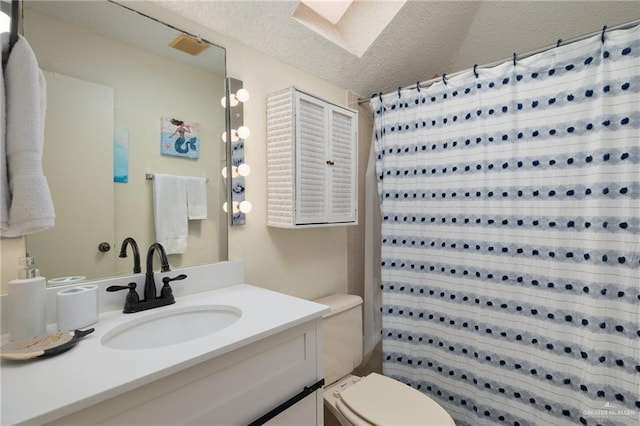 full bath with a textured ceiling, toilet, a skylight, vanity, and tiled shower