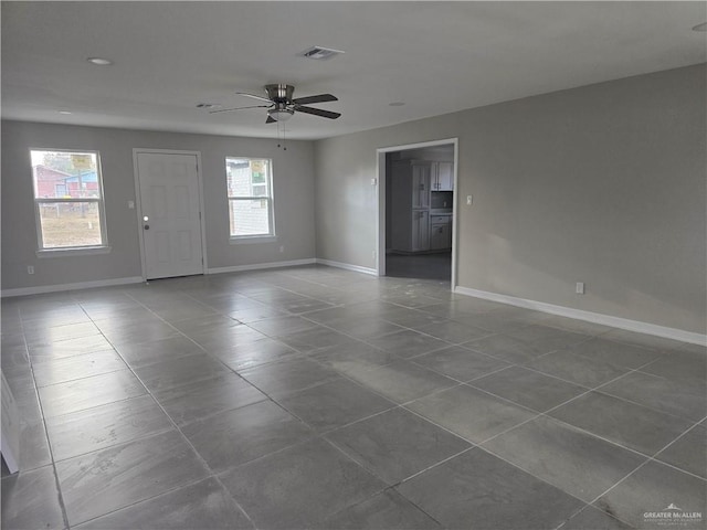 empty room with visible vents, a healthy amount of sunlight, a ceiling fan, and baseboards