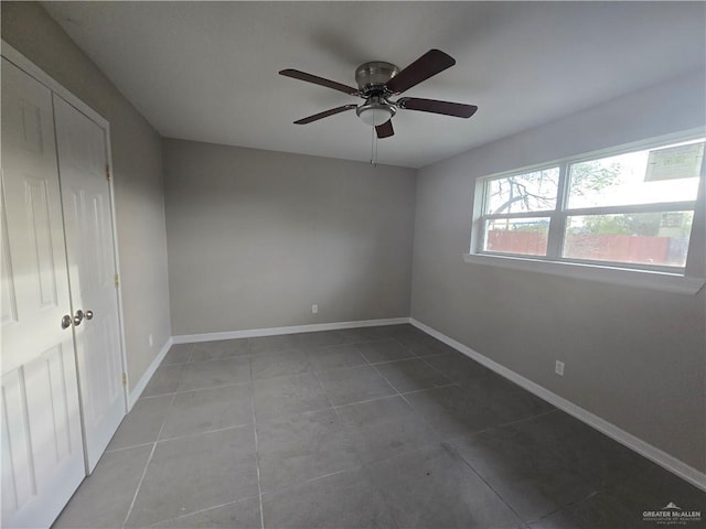 tiled empty room featuring a ceiling fan and baseboards