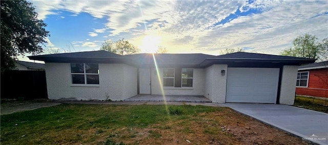 single story home featuring a front lawn, concrete driveway, brick siding, and a garage