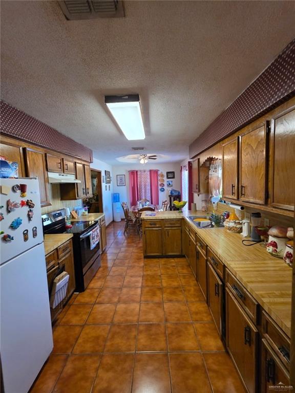 kitchen with stainless steel range with electric cooktop, freestanding refrigerator, a peninsula, visible vents, and under cabinet range hood