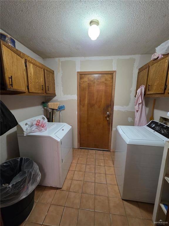 washroom with washer and dryer, a textured ceiling, light tile patterned floors, and cabinet space