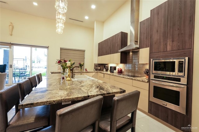 kitchen featuring wall chimney exhaust hood, modern cabinets, a sink, stainless steel appliances, and backsplash