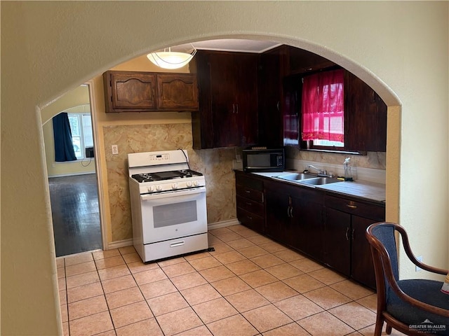 kitchen featuring dark brown cabinetry, sink, white gas stove, and light tile patterned flooring