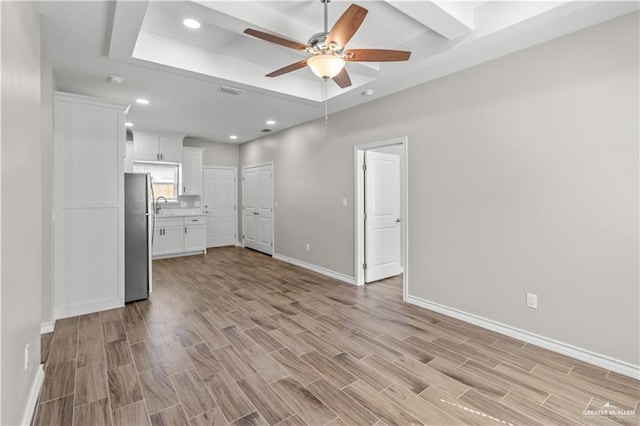 unfurnished living room with ceiling fan, a raised ceiling, and light hardwood / wood-style flooring