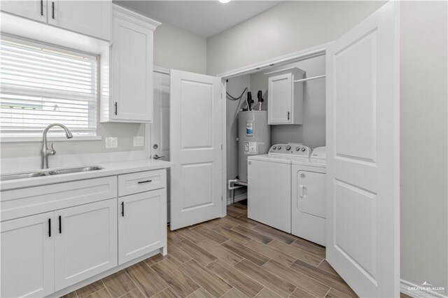 washroom featuring cabinets, electric water heater, washer and clothes dryer, sink, and light hardwood / wood-style floors