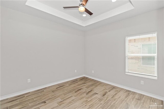 unfurnished room featuring light hardwood / wood-style floors, ceiling fan, and a tray ceiling