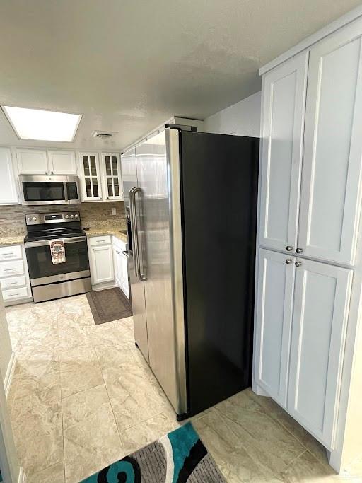 kitchen with tasteful backsplash, white cabinetry, stainless steel appliances, and light stone counters