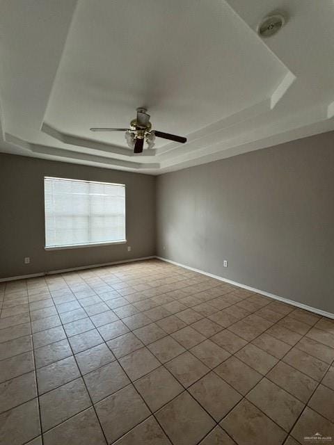 empty room featuring ceiling fan, light tile patterned flooring, and a raised ceiling