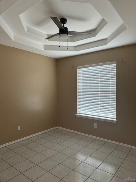 tiled empty room with ceiling fan and a tray ceiling