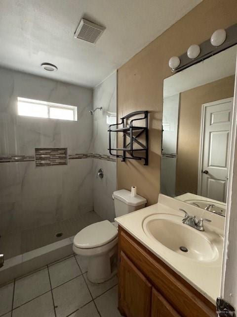 bathroom with tiled shower, vanity, tile patterned floors, and toilet