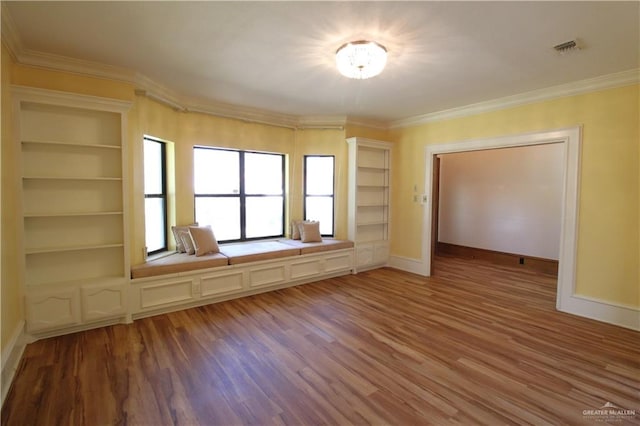 spare room featuring hardwood / wood-style flooring, built in shelves, and crown molding