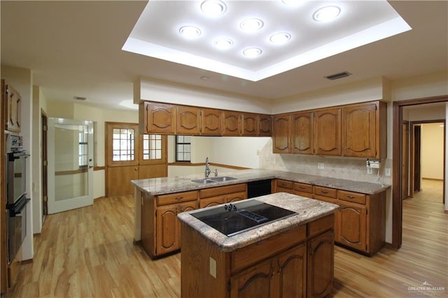 kitchen with kitchen peninsula, black electric cooktop, a raised ceiling, sink, and a center island