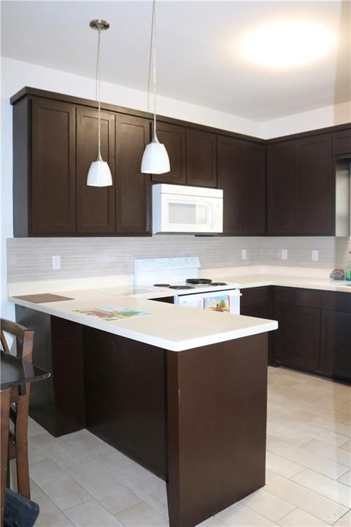 kitchen with hanging light fixtures, tasteful backsplash, white appliances, and kitchen peninsula