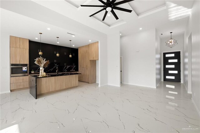 kitchen featuring a center island, oven, ceiling fan, light brown cabinetry, and decorative light fixtures