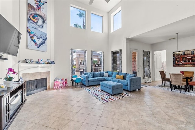 tiled living room featuring ceiling fan, a towering ceiling, and a tiled fireplace