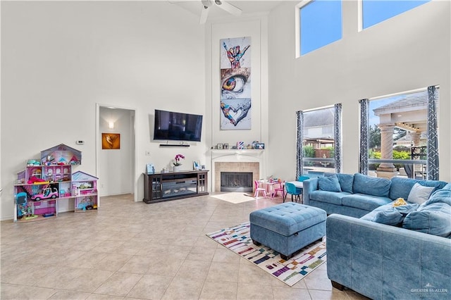 tiled living room with a tiled fireplace, ceiling fan, and a high ceiling